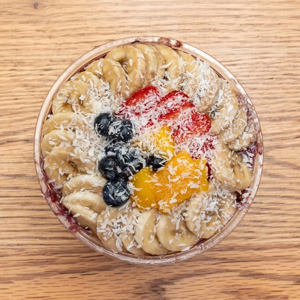 Overhead view of an acai bowl with bananas, blueberries, strawberries, mango, and shredded coconut.