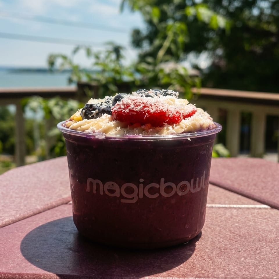 Magic Bowl acai bowl with berries, bananas, and coconut flakes on a patio table overlooking the ocean.