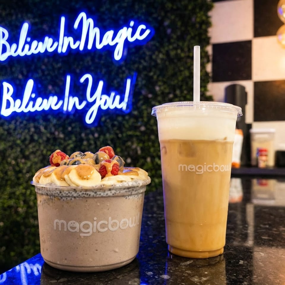 Magic Bowl smoothie bowl with fruit and a cold drink on a counter with a neon sign.